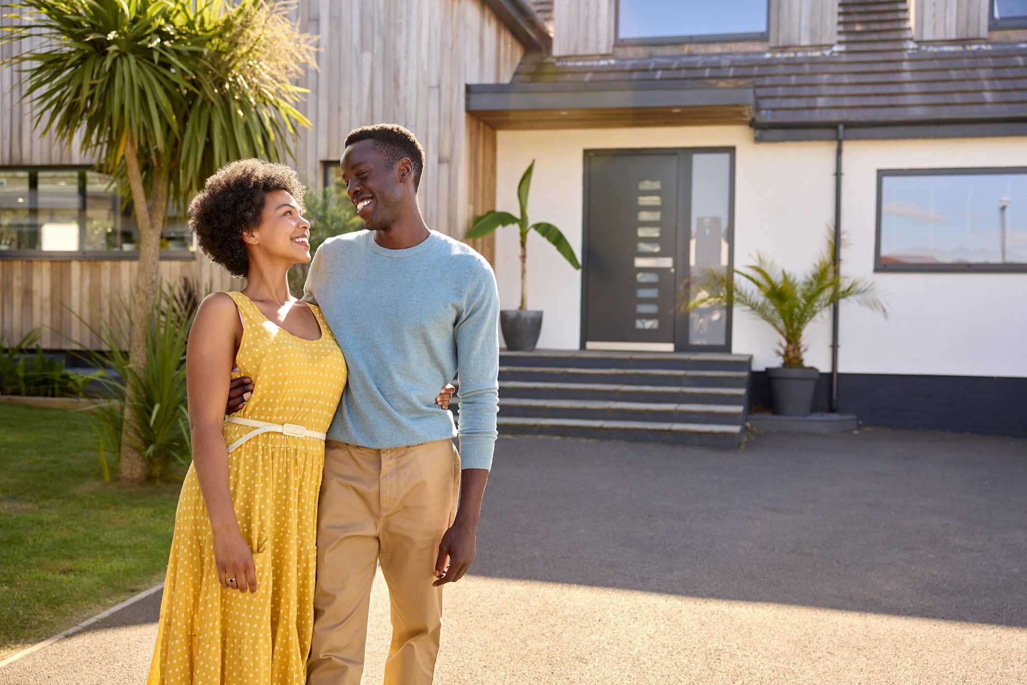Portrait Of Couple Standing In Driveway In Front Of Dream Home Together